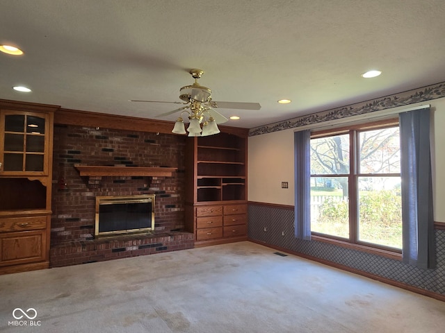 unfurnished living room with a textured ceiling, a brick fireplace, ceiling fan, and carpet flooring