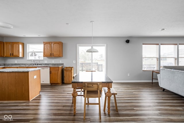 kitchen featuring light stone counters, white dishwasher, dark wood-type flooring, sink, and decorative light fixtures