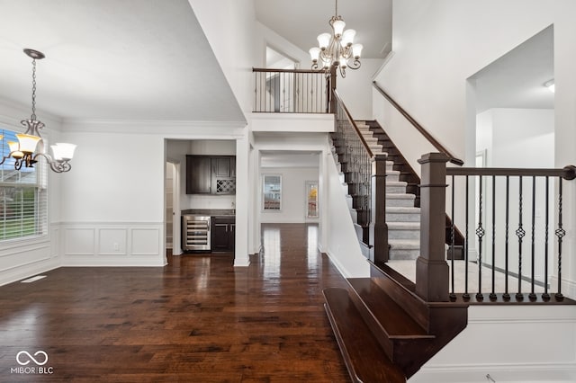 stairway featuring hardwood / wood-style floors, wine cooler, a towering ceiling, ornamental molding, and a chandelier