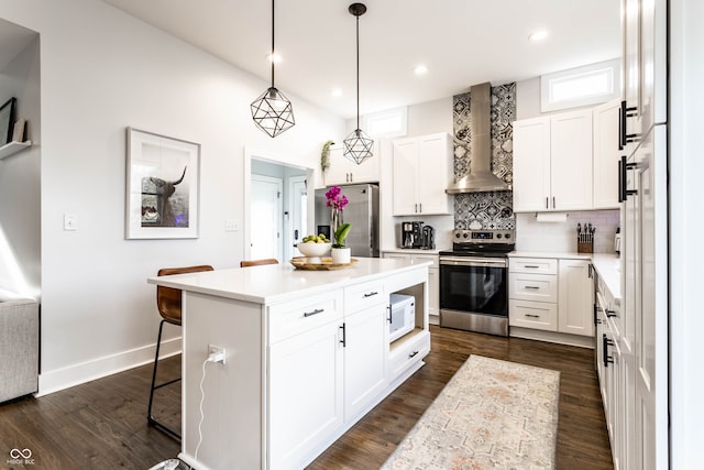 kitchen featuring a center island, wall chimney exhaust hood, stainless steel appliances, a kitchen bar, and white cabinets