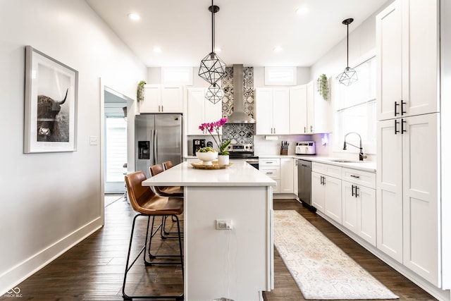 kitchen with appliances with stainless steel finishes, wall chimney exhaust hood, sink, white cabinetry, and hanging light fixtures