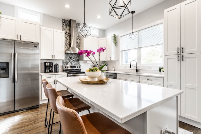 kitchen featuring sink, wall chimney range hood, decorative light fixtures, white cabinets, and appliances with stainless steel finishes