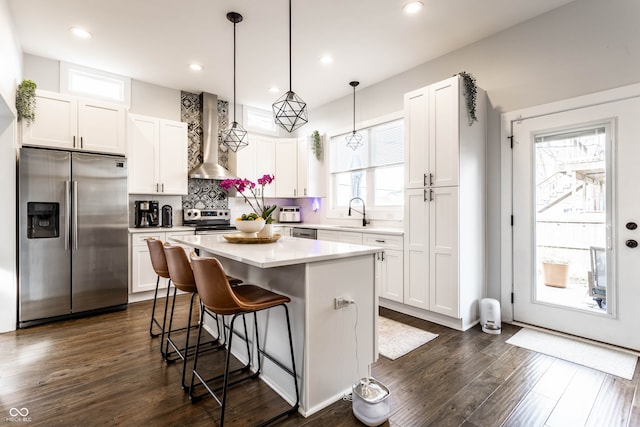 kitchen featuring appliances with stainless steel finishes, wall chimney exhaust hood, pendant lighting, a center island, and white cabinetry