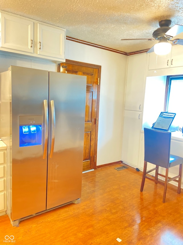 kitchen featuring stainless steel fridge, light wood-type flooring, ceiling fan, crown molding, and white cabinetry