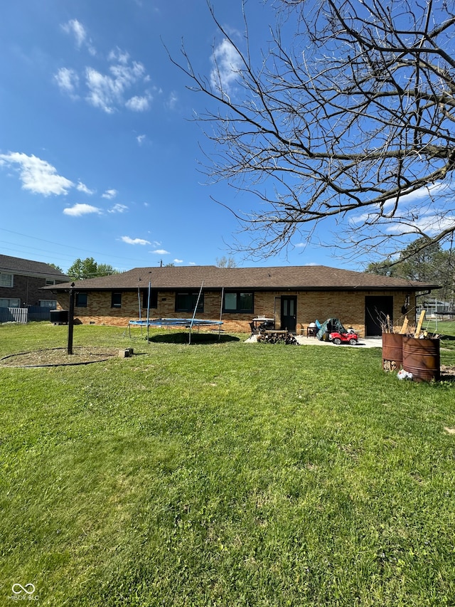 rear view of property featuring a patio area, a yard, and a trampoline