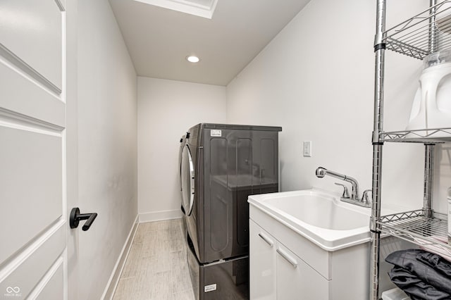 laundry area with cabinets, light wood-type flooring, washing machine and dryer, and sink