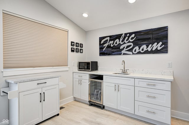 bar featuring sink, white cabinets, light hardwood / wood-style floors, and lofted ceiling