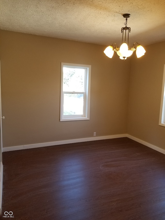 empty room featuring a notable chandelier, dark hardwood / wood-style floors, and a textured ceiling