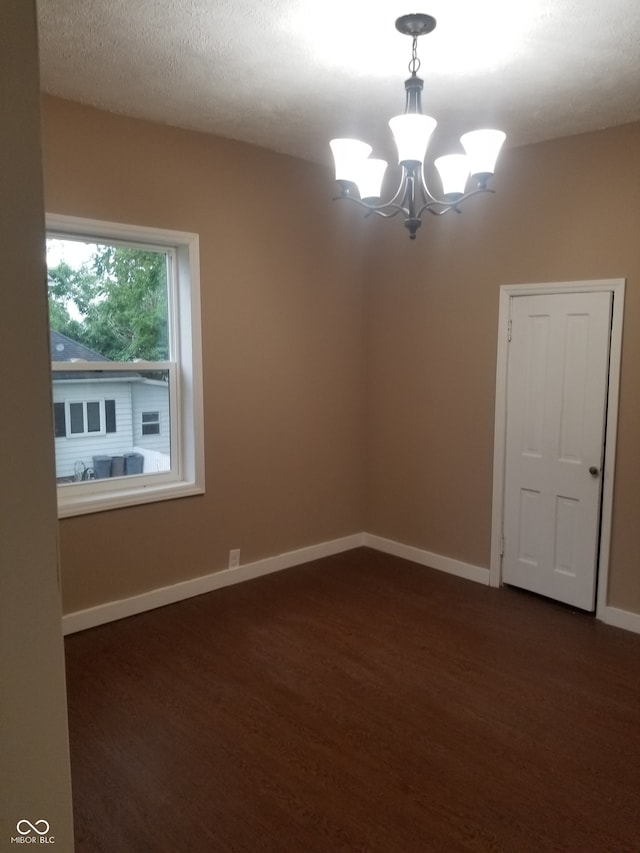 spare room with a textured ceiling, dark hardwood / wood-style floors, and an inviting chandelier