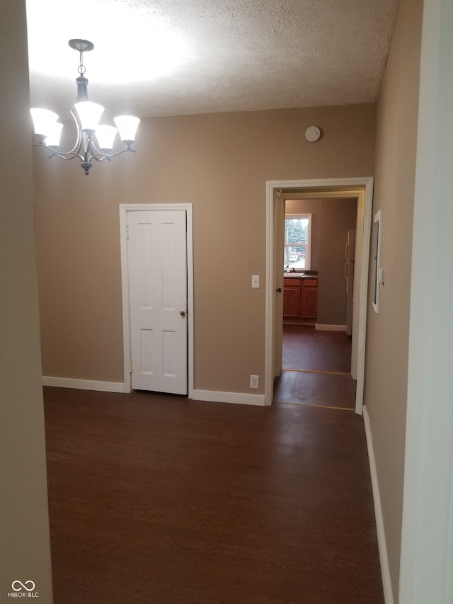 empty room featuring a notable chandelier, dark hardwood / wood-style flooring, and a textured ceiling