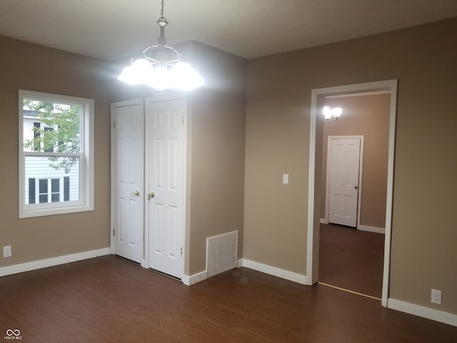 unfurnished bedroom with a chandelier and dark wood-type flooring