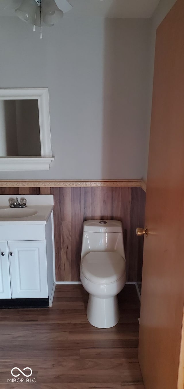 bathroom featuring wood-type flooring, vanity, toilet, and wood walls