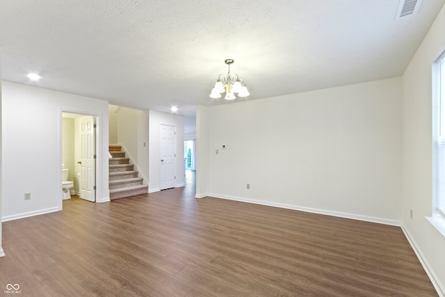 spare room with a textured ceiling, a notable chandelier, and dark wood-type flooring