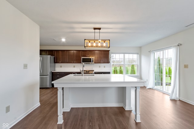 kitchen featuring an island with sink, tasteful backsplash, decorative light fixtures, dark hardwood / wood-style flooring, and stainless steel appliances