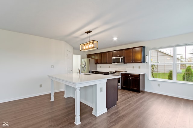 kitchen featuring a kitchen island with sink, dark wood-type flooring, hanging light fixtures, decorative backsplash, and stainless steel appliances