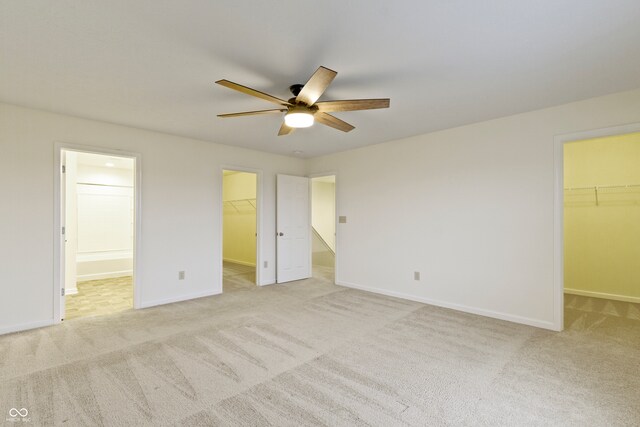 unfurnished bedroom featuring light carpet, ensuite bath, a spacious closet, and ceiling fan