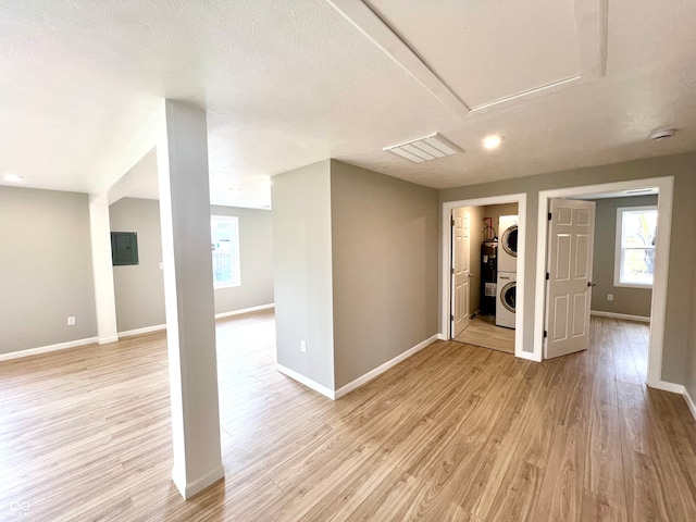 spare room with a textured ceiling, light wood-type flooring, stacked washing maching and dryer, and electric water heater