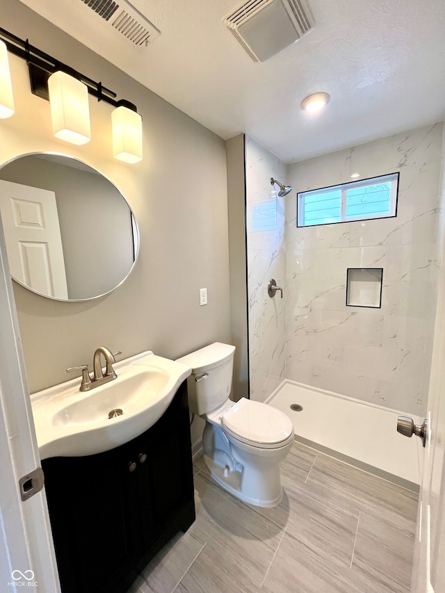 bathroom with vanity, toilet, and a tile shower