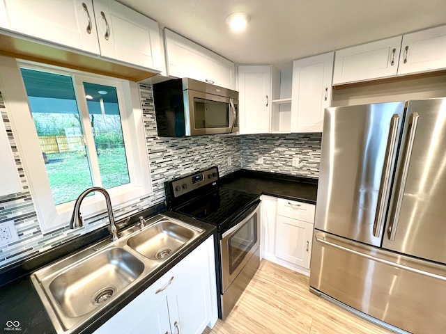 kitchen featuring appliances with stainless steel finishes, light wood-type flooring, tasteful backsplash, sink, and white cabinets