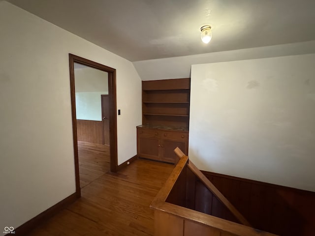 corridor featuring lofted ceiling, wooden walls, and dark wood-type flooring