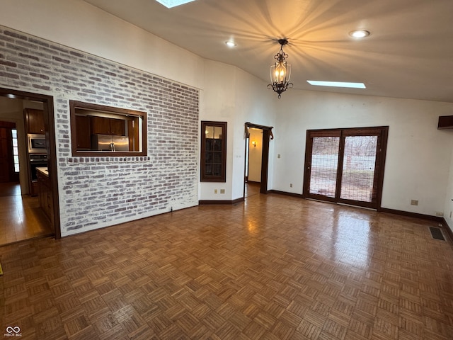 unfurnished living room featuring high vaulted ceiling, brick wall, and a chandelier