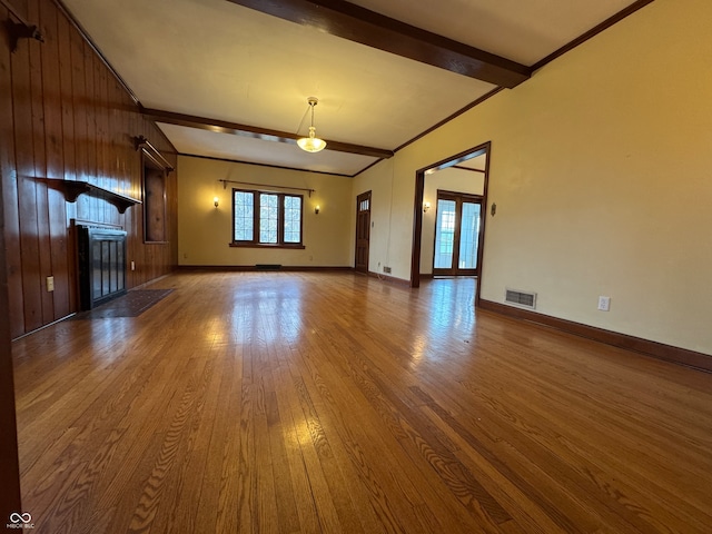 unfurnished living room featuring beamed ceiling, wood-type flooring, ornamental molding, and wood walls