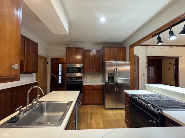 kitchen with sink, tasteful backsplash, crown molding, black appliances, and light wood-type flooring