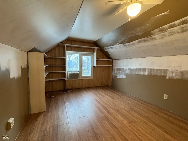 additional living space with light wood-type flooring, cooling unit, wooden walls, ceiling fan, and lofted ceiling