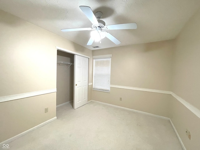 unfurnished bedroom featuring ceiling fan, light colored carpet, a textured ceiling, and a closet