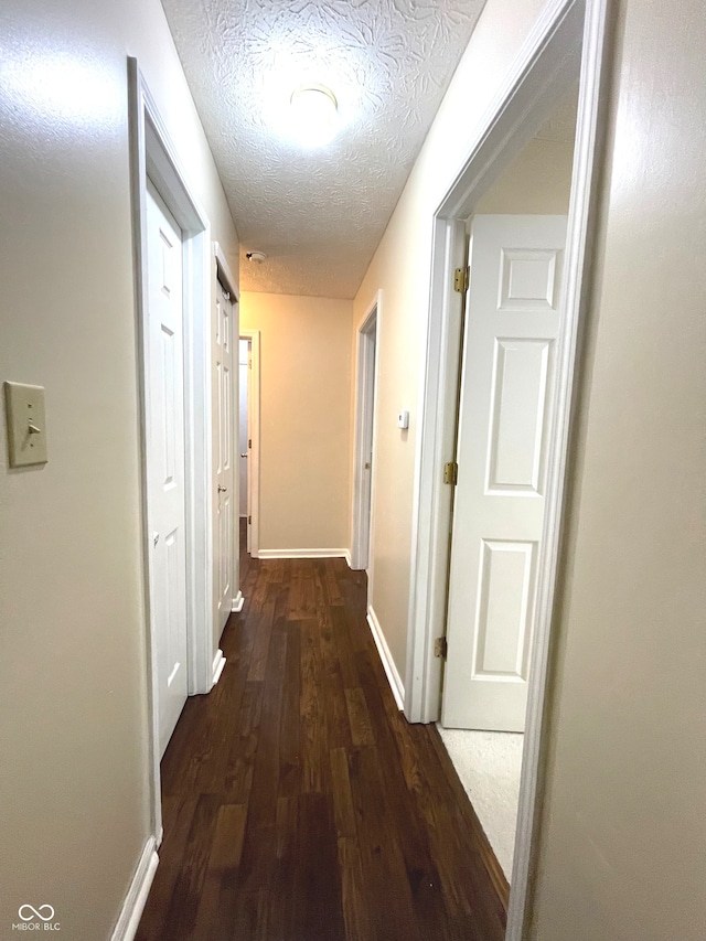 corridor with a textured ceiling and dark wood-type flooring