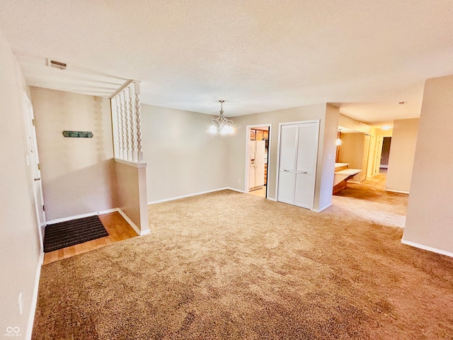 carpeted spare room featuring a chandelier and a textured ceiling