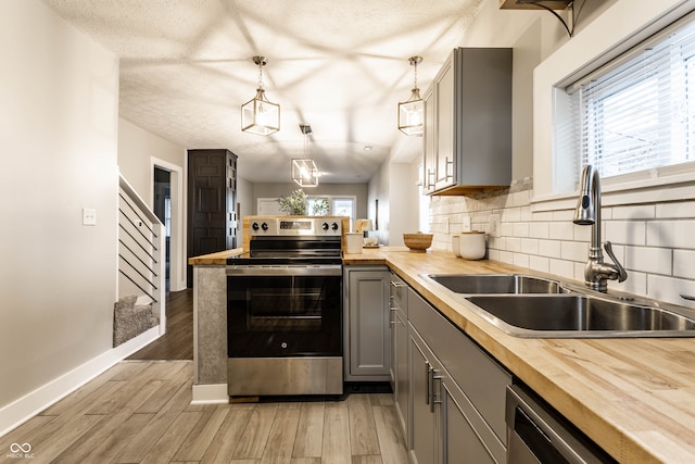 kitchen with wooden counters, stainless steel appliances, sink, pendant lighting, and gray cabinets