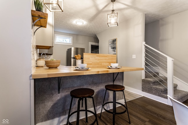 kitchen with a textured ceiling, a breakfast bar area, dark hardwood / wood-style floors, stainless steel refrigerator, and butcher block counters