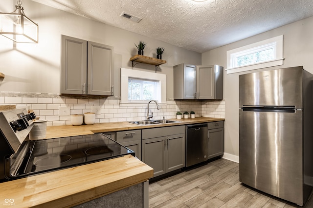 kitchen with a healthy amount of sunlight, sink, wooden counters, and appliances with stainless steel finishes