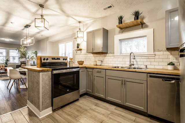 kitchen featuring wooden counters, stainless steel appliances, hanging light fixtures, and sink