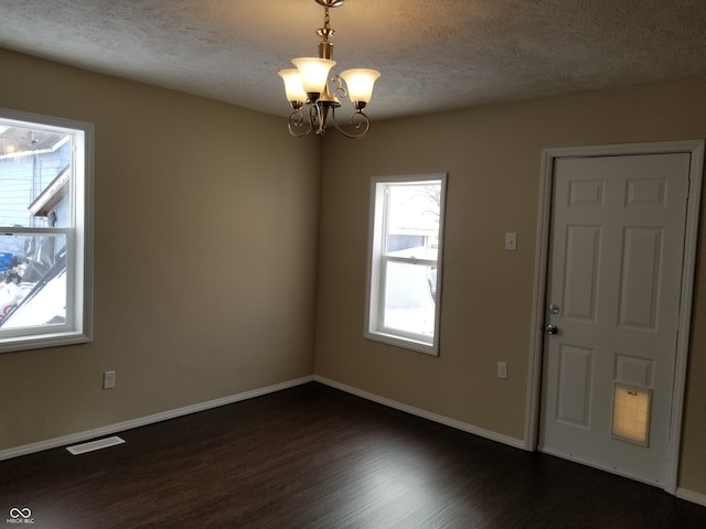 empty room with a chandelier, a textured ceiling, and dark hardwood / wood-style flooring