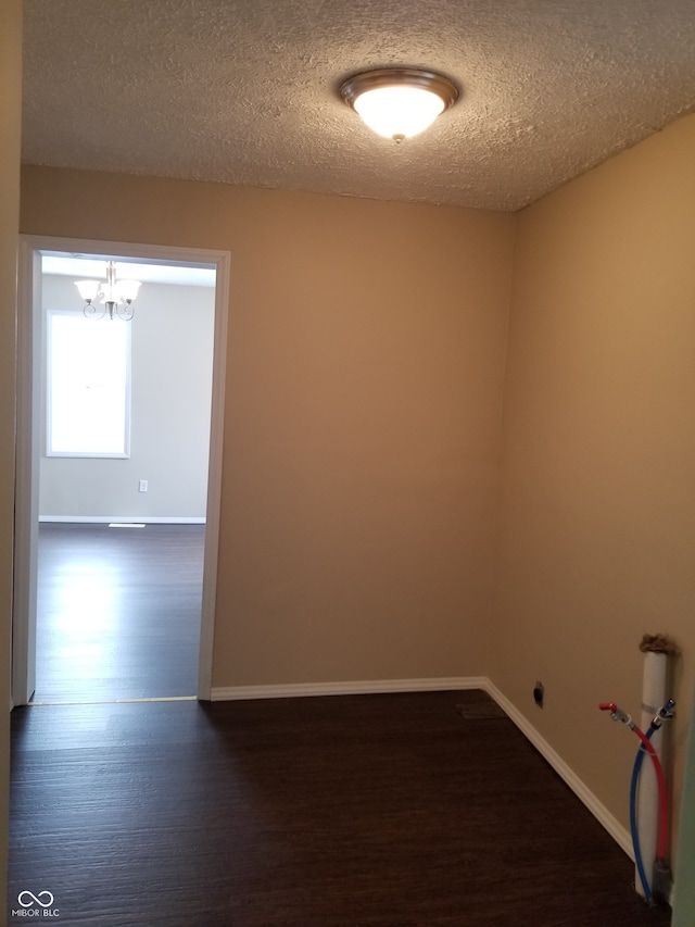 unfurnished room featuring a textured ceiling, dark wood-type flooring, and a notable chandelier