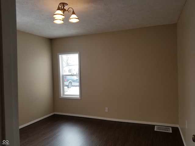 empty room with a notable chandelier, dark hardwood / wood-style floors, and a textured ceiling