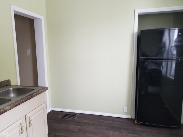 kitchen featuring white cabinets, black refrigerator, sink, and dark wood-type flooring