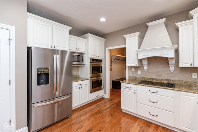 kitchen featuring premium range hood, white cabinetry, appliances with stainless steel finishes, light wood-type flooring, and tasteful backsplash