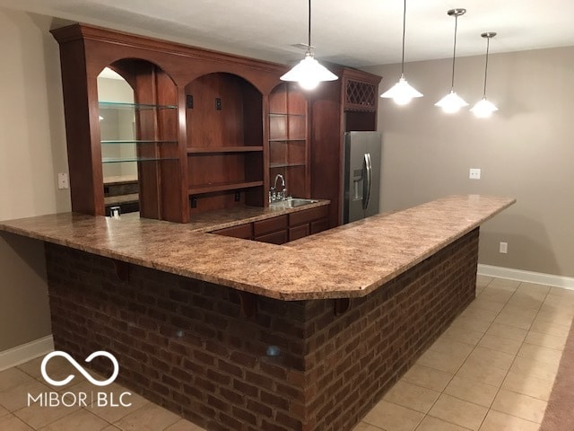 bar featuring hanging light fixtures, a sink, stainless steel refrigerator with ice dispenser, indoor wet bar, and light tile patterned flooring