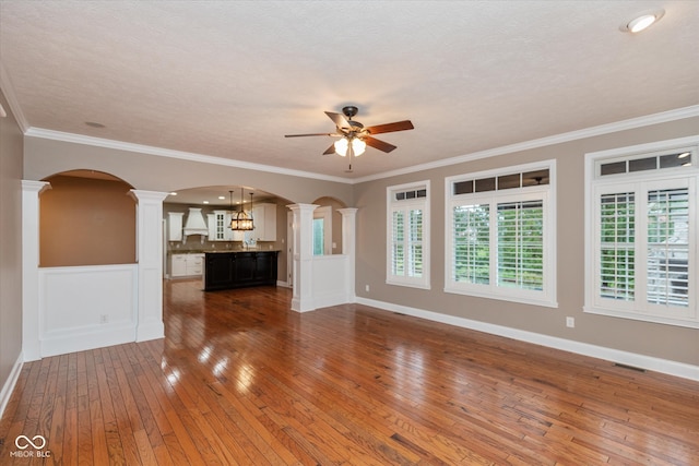 unfurnished living room with ornamental molding, arched walkways, ornate columns, and hardwood / wood-style flooring