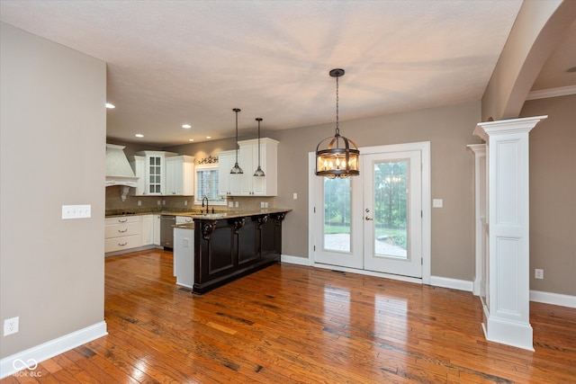 kitchen featuring glass insert cabinets, white cabinetry, a sink, a peninsula, and ornate columns