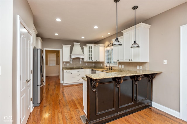 kitchen featuring stainless steel refrigerator with ice dispenser, custom exhaust hood, decorative backsplash, a sink, and a peninsula