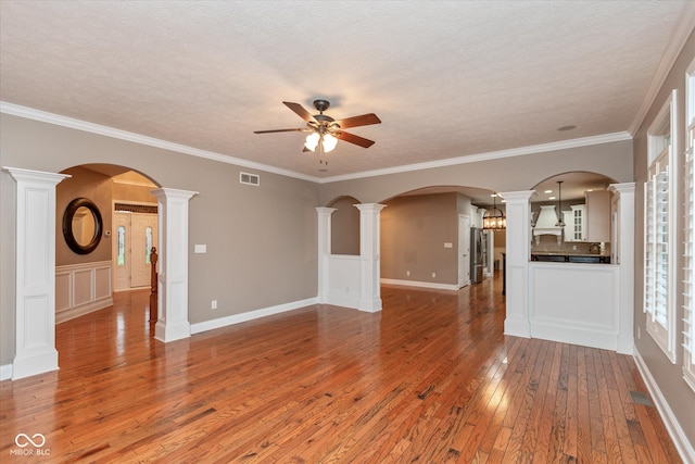 unfurnished living room featuring arched walkways, a textured ceiling, visible vents, light wood-style floors, and ornate columns