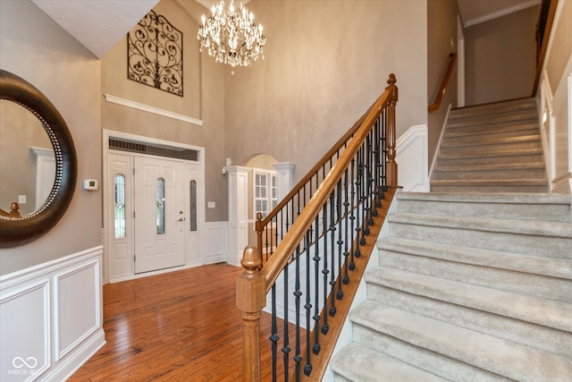 entrance foyer with wood-type flooring, a decorative wall, wainscoting, a chandelier, and ornate columns