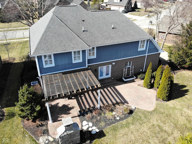 rear view of house with brick siding, a shingled roof, a lawn, and french doors