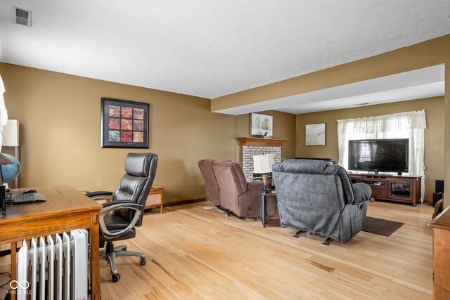 office with a fireplace, radiator heating unit, and light hardwood / wood-style flooring