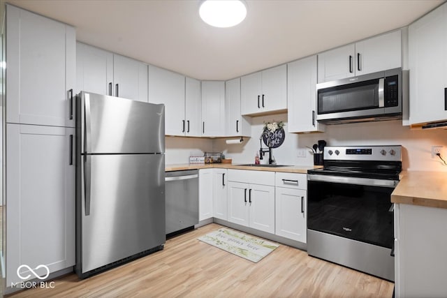 kitchen featuring sink, stainless steel appliances, wood counters, light hardwood / wood-style flooring, and white cabinets