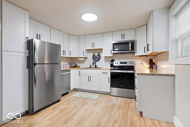 kitchen featuring white cabinetry, sink, light hardwood / wood-style floors, and appliances with stainless steel finishes